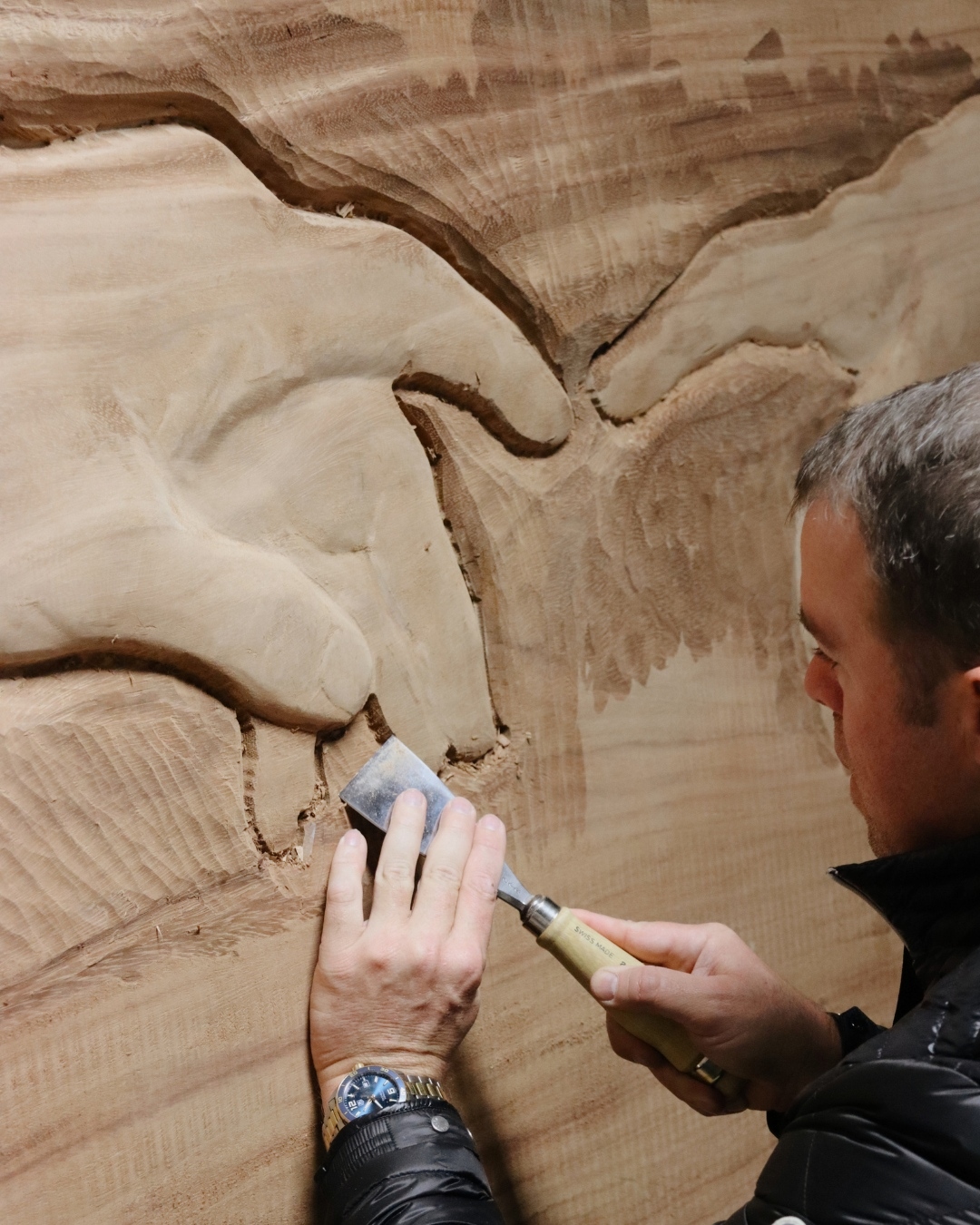 Hand carving relief into a large wood slab with chisels