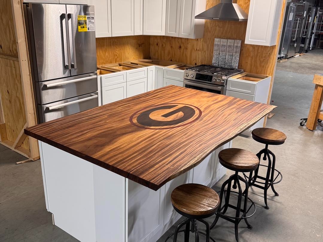 Kitchen island with a dark wood slab top and an inlaid oval G logo, with bar stools